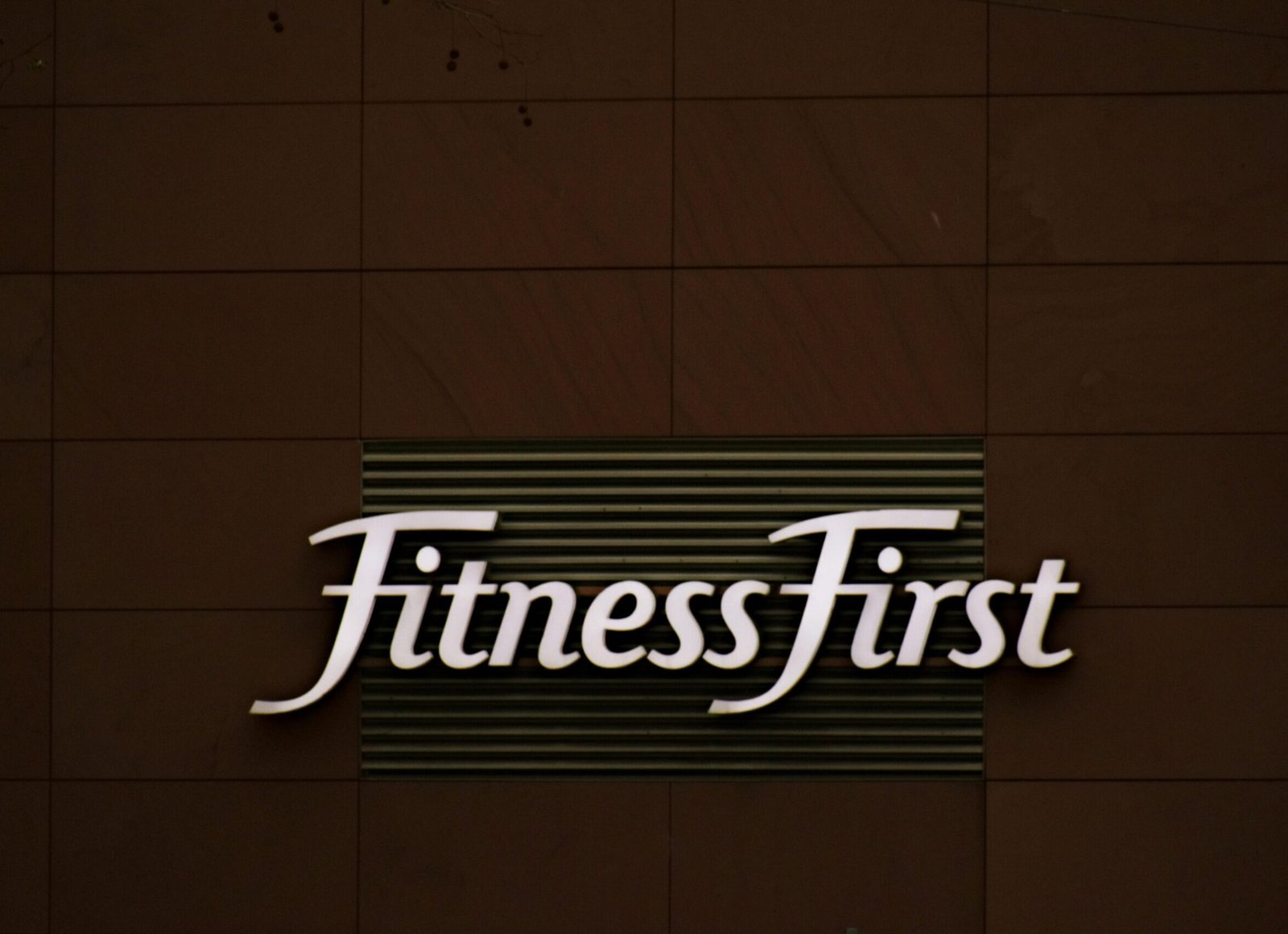 Close-up of FitnessFirst gym sign on a contemporary brown wall.